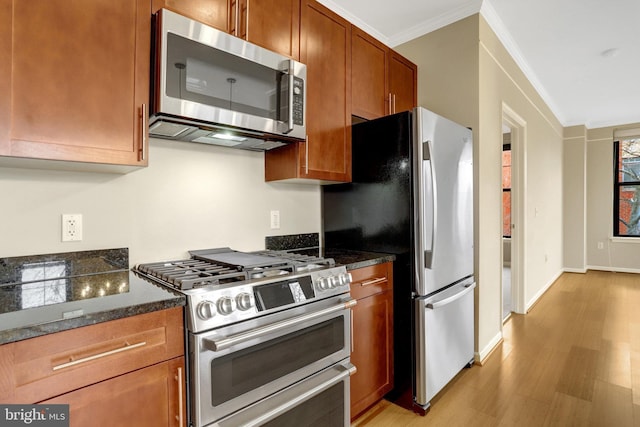 kitchen with light wood-style flooring, stainless steel appliances, brown cabinets, dark stone counters, and crown molding