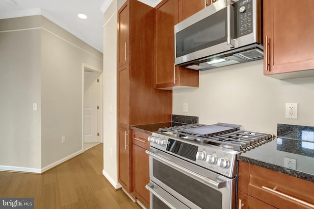 kitchen featuring light wood-style flooring, appliances with stainless steel finishes, brown cabinetry, dark stone counters, and baseboards