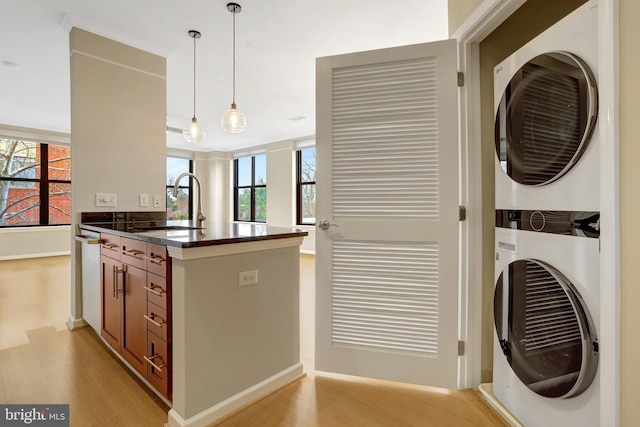 kitchen featuring brown cabinets, decorative light fixtures, stacked washer / drying machine, light wood-style floors, and a sink