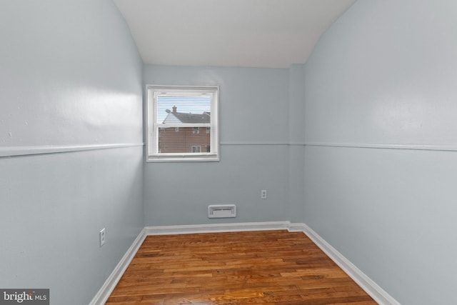 spare room with baseboards, vaulted ceiling, and wood finished floors