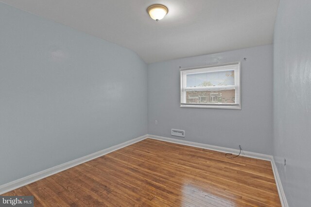 empty room featuring baseboards, vaulted ceiling, and wood finished floors