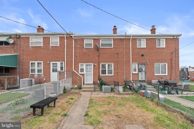 rear view of house with central AC, a chimney, and fence