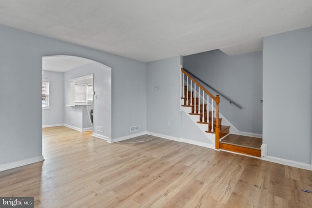 unfurnished living room featuring visible vents, stairs, wood finished floors, baseboards, and arched walkways