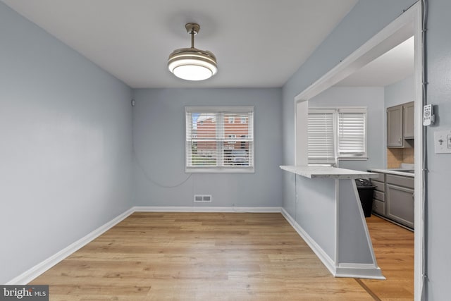 unfurnished dining area featuring light wood-type flooring, baseboards, and visible vents