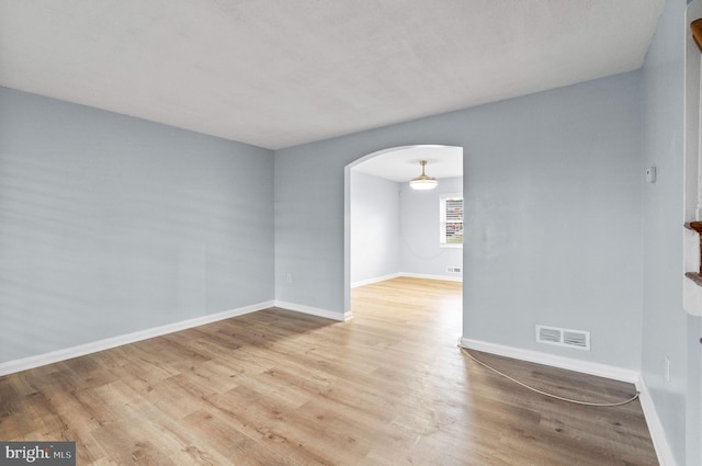 empty room featuring arched walkways, baseboards, wood finished floors, and visible vents