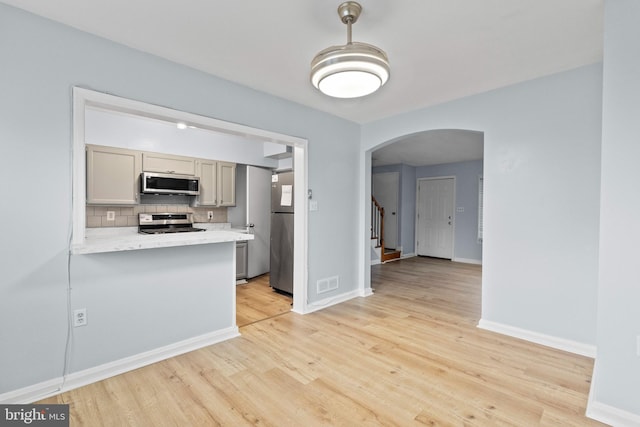 kitchen with arched walkways, light wood finished floors, appliances with stainless steel finishes, and tasteful backsplash