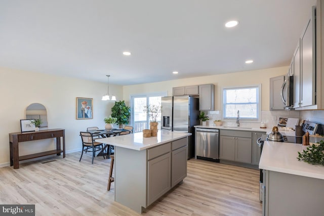 kitchen with stainless steel appliances, backsplash, gray cabinetry, a sink, and a kitchen breakfast bar