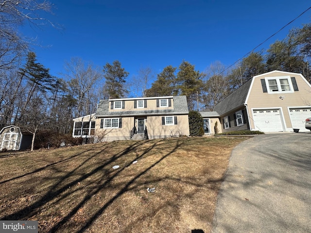 view of front of home with driveway, a gambrel roof, an outdoor structure, a storage unit, and a garage