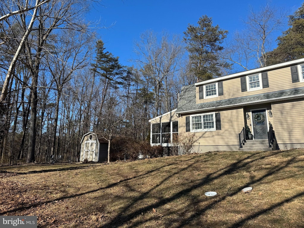 view of side of property featuring a lawn, a storage shed, entry steps, a sunroom, and an outdoor structure