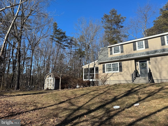 view of side of property featuring a lawn, a storage shed, entry steps, a sunroom, and an outdoor structure