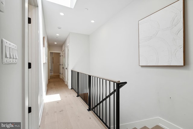 corridor with a skylight, baseboards, an upstairs landing, light wood-style floors, and recessed lighting