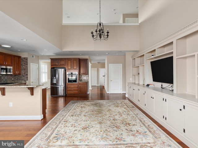 kitchen featuring dark wood-type flooring, appliances with stainless steel finishes, light stone countertops, brown cabinetry, and a kitchen bar