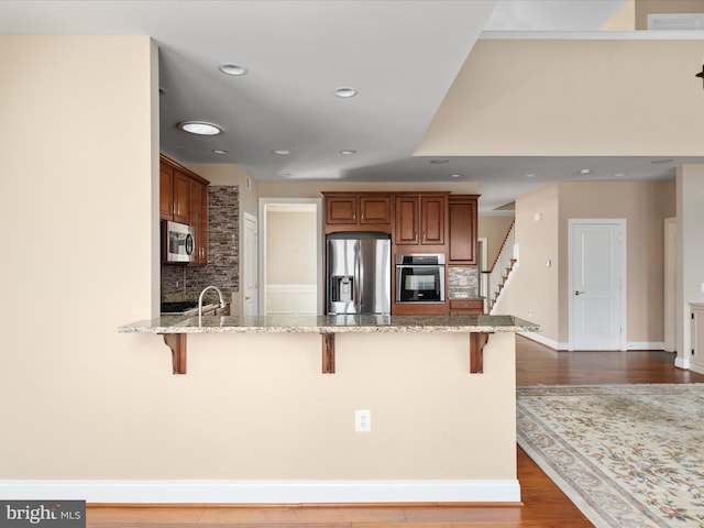 kitchen with appliances with stainless steel finishes, a breakfast bar, a peninsula, and light stone counters