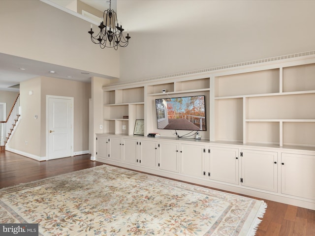 unfurnished living room featuring baseboards, a towering ceiling, dark wood-type flooring, an inviting chandelier, and stairs