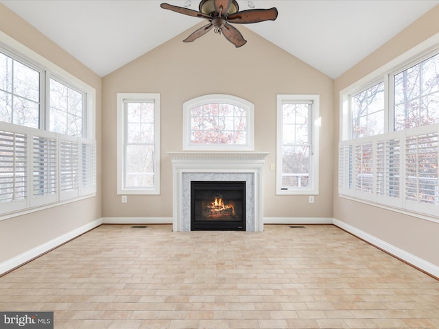 unfurnished living room with ceiling fan, vaulted ceiling, a glass covered fireplace, and baseboards