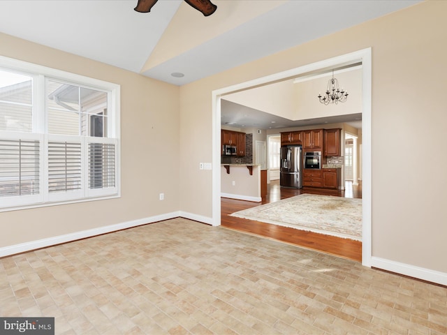 unfurnished living room featuring lofted ceiling, ceiling fan with notable chandelier, and baseboards