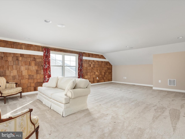 living room with lofted ceiling, wooden walls, visible vents, baseboards, and carpet