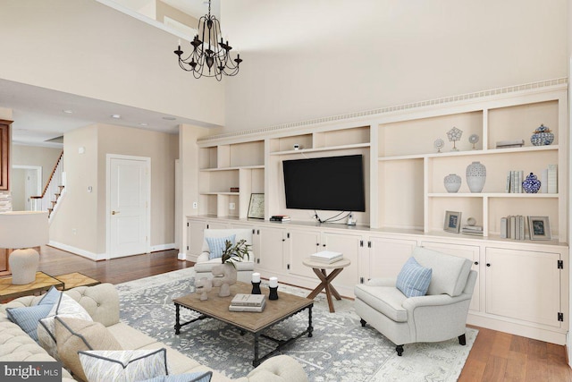 living area featuring baseboards, stairway, wood finished floors, an inviting chandelier, and a high ceiling