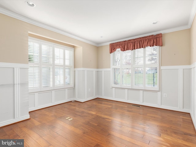 spare room with ornamental molding, visible vents, a decorative wall, and hardwood / wood-style flooring