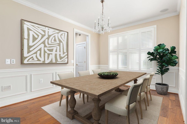 dining area with visible vents, a wainscoted wall, ornamental molding, wood finished floors, and a chandelier