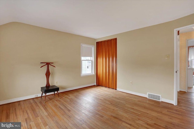 empty room with baseboards, visible vents, vaulted ceiling, and light wood finished floors