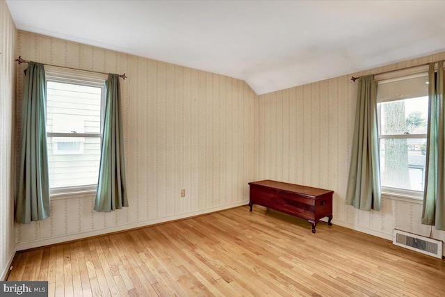 living area with wallpapered walls, baseboards, visible vents, vaulted ceiling, and light wood-type flooring