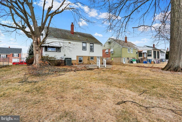 back of house featuring fence, a yard, a chimney, and central AC unit