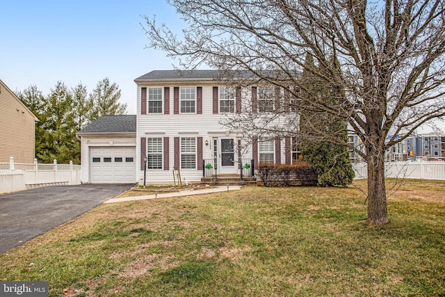 colonial house featuring a shingled roof, a front lawn, fence, a garage, and driveway