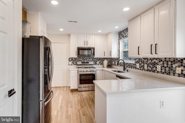 kitchen with light wood finished floors, a peninsula, a sink, stainless steel appliances, and light countertops