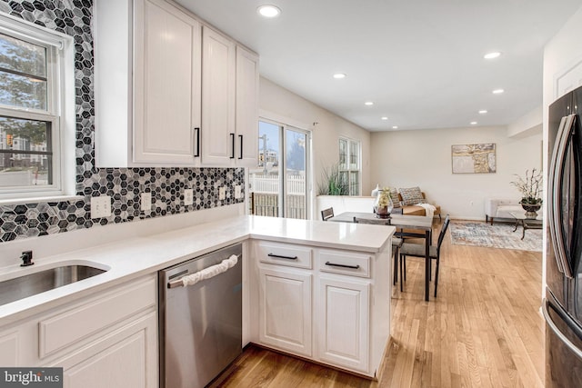 kitchen with appliances with stainless steel finishes, light countertops, light wood-type flooring, and a peninsula