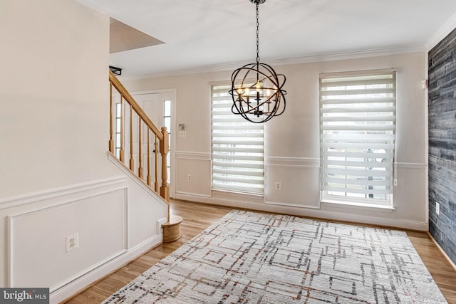 foyer entrance featuring stairway, wainscoting, crown molding, light wood-type flooring, and a chandelier