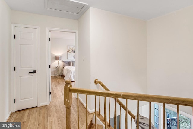 hall featuring attic access, light wood-style flooring, an upstairs landing, and baseboards