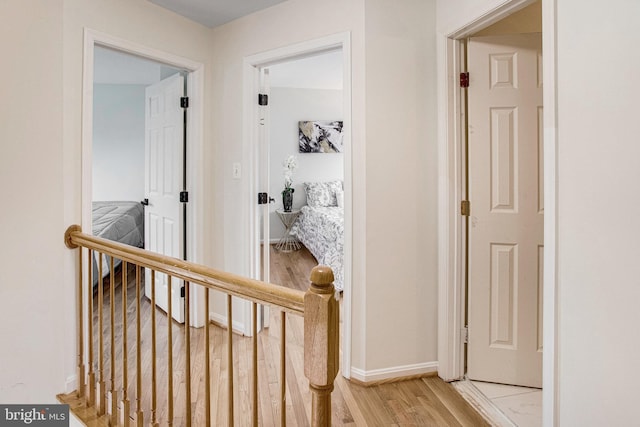 hallway featuring an upstairs landing, baseboards, and light wood-type flooring