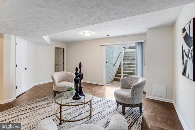 sitting room with dark wood finished floors, a textured ceiling, stairs, and baseboards