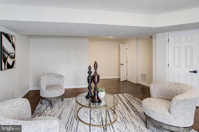 living area with visible vents, a textured ceiling, baseboards, and wood finished floors