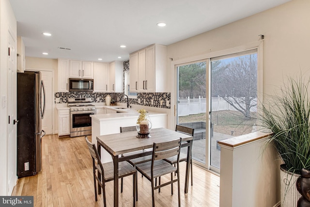 kitchen with a sink, stainless steel appliances, light wood-style floors, light countertops, and decorative backsplash