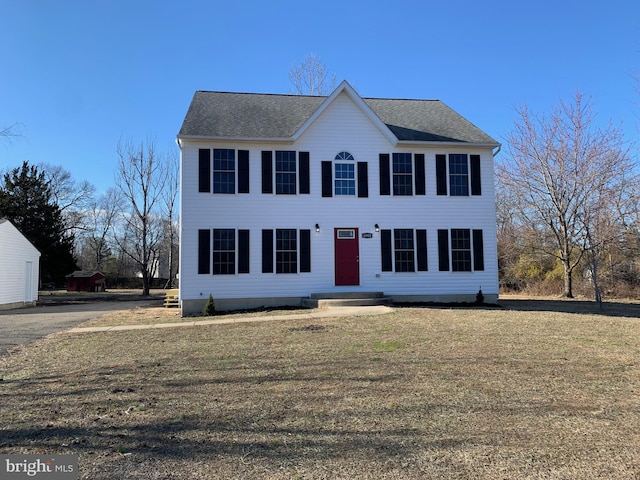 colonial house featuring a front yard and roof with shingles