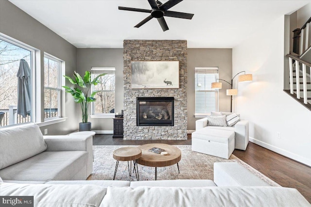 living area with wood finished floors, baseboards, a fireplace, ceiling fan, and stairs