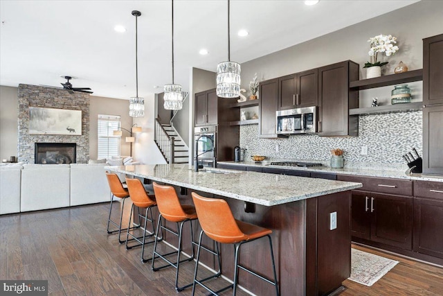 kitchen featuring dark brown cabinetry, a stone fireplace, stainless steel appliances, and open shelves