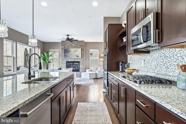 kitchen featuring tasteful backsplash, dark brown cabinets, a fireplace, stainless steel appliances, and a sink