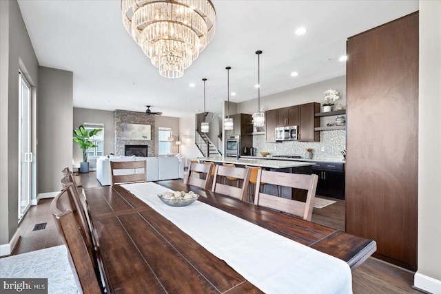 dining room with visible vents, dark wood-type flooring, stairs, a stone fireplace, and recessed lighting