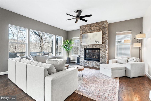 living area featuring baseboards, dark wood-type flooring, and a stone fireplace