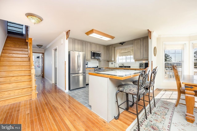 kitchen with ornamental molding, a center island, appliances with stainless steel finishes, light wood finished floors, and light countertops