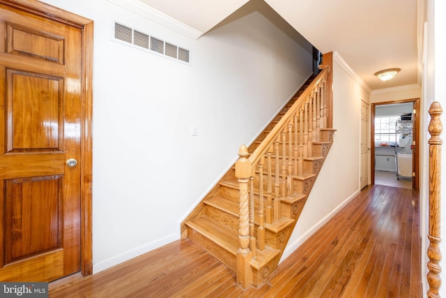 stairs with visible vents, baseboards, crown molding, and hardwood / wood-style flooring