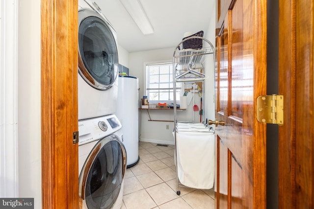 laundry room with water heater, stacked washing maching and dryer, light tile patterned flooring, baseboards, and laundry area