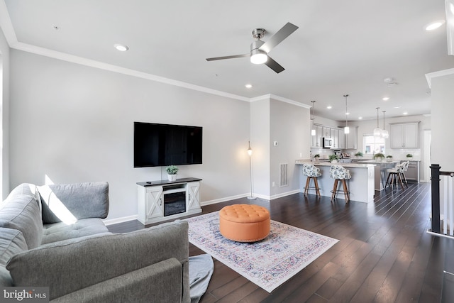 living room with ornamental molding, dark wood-style flooring, visible vents, and baseboards