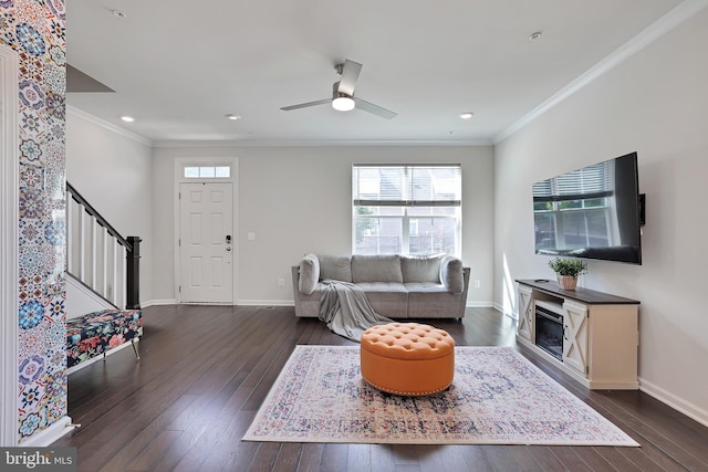 living area featuring a ceiling fan, baseboards, stairs, ornamental molding, and dark wood finished floors