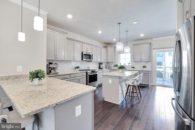 kitchen with decorative backsplash, appliances with stainless steel finishes, dark wood-type flooring, a peninsula, and a kitchen bar