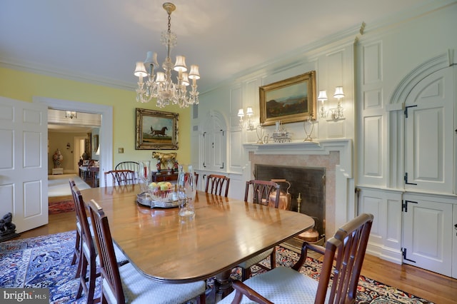 dining space featuring wood finished floors, an inviting chandelier, ornamental molding, and a high end fireplace