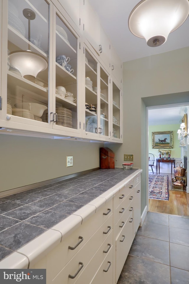 kitchen with tile patterned floors, white cabinets, glass insert cabinets, and tile counters